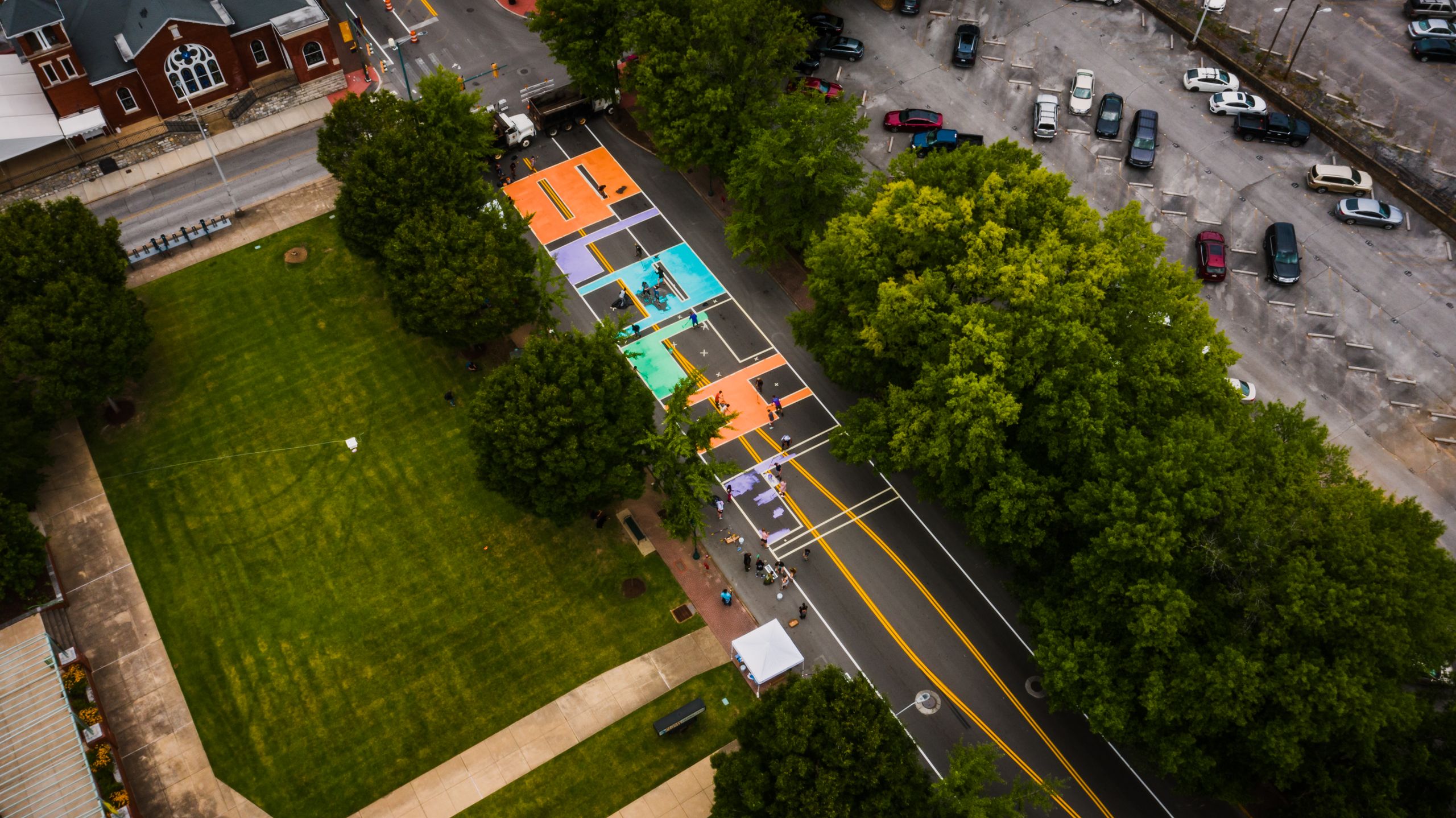 Drone view of narrow roadway with bright letters near grass meadow with trees and parking with transport