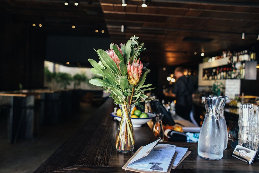 Elegant bar counter with protea flowers, glassware, and menu creating a cozy atmosphere.