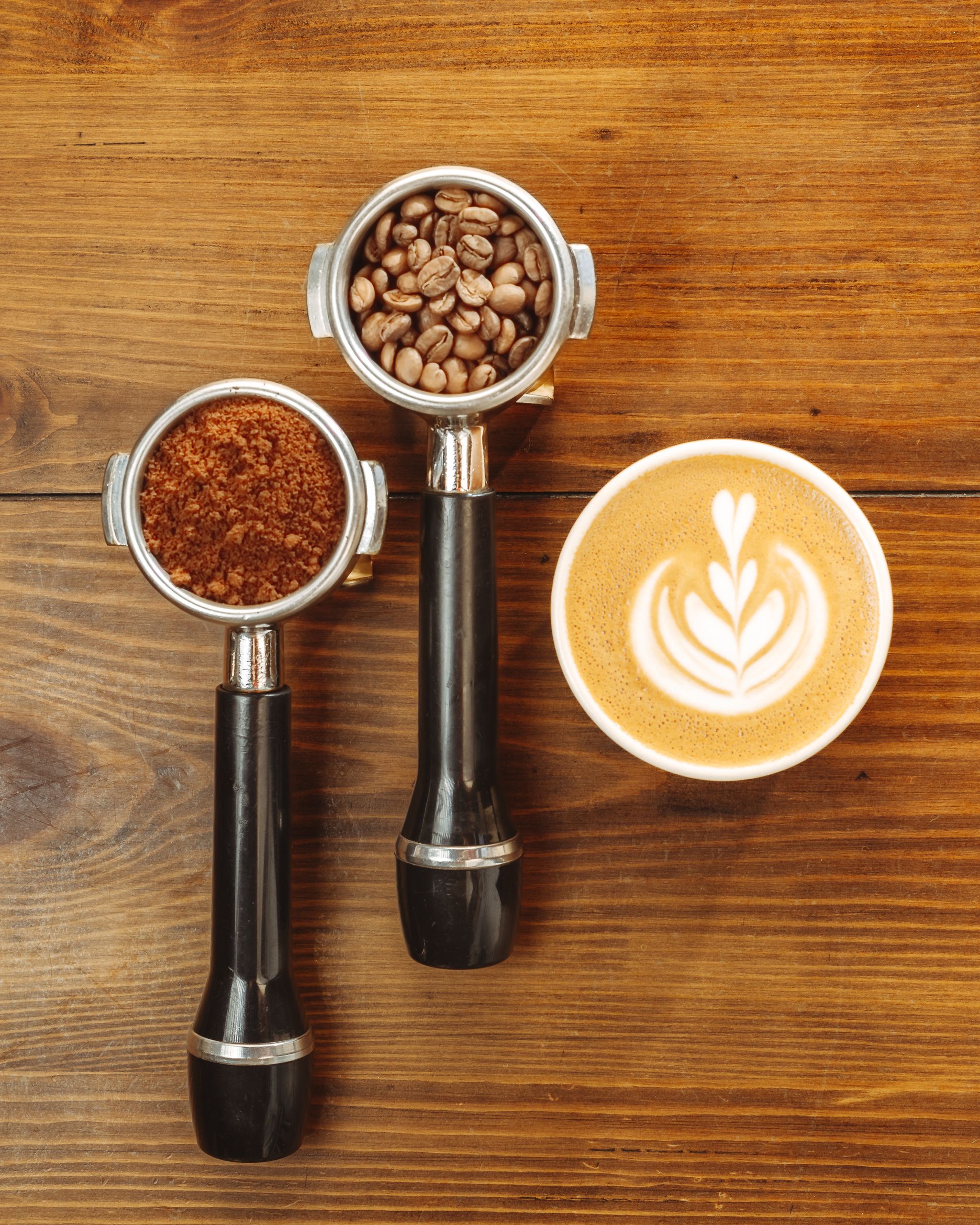 Espresso portafilters with coffee beans and latte art on wood surface.