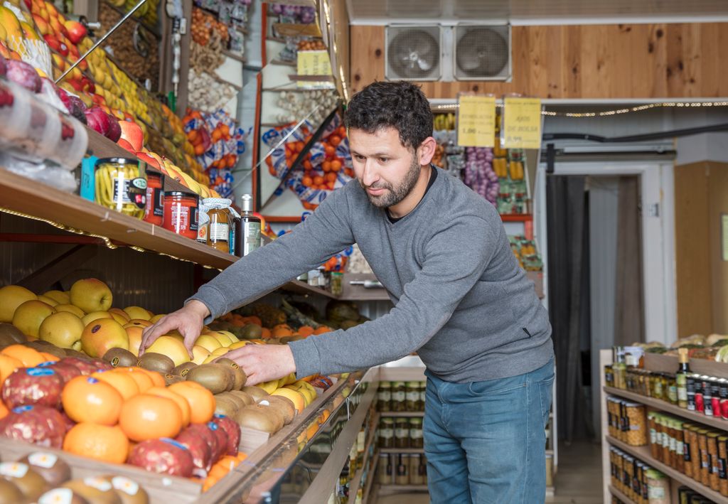 Grocery store worker organizing fresh fruits and vegetables on display shelves.