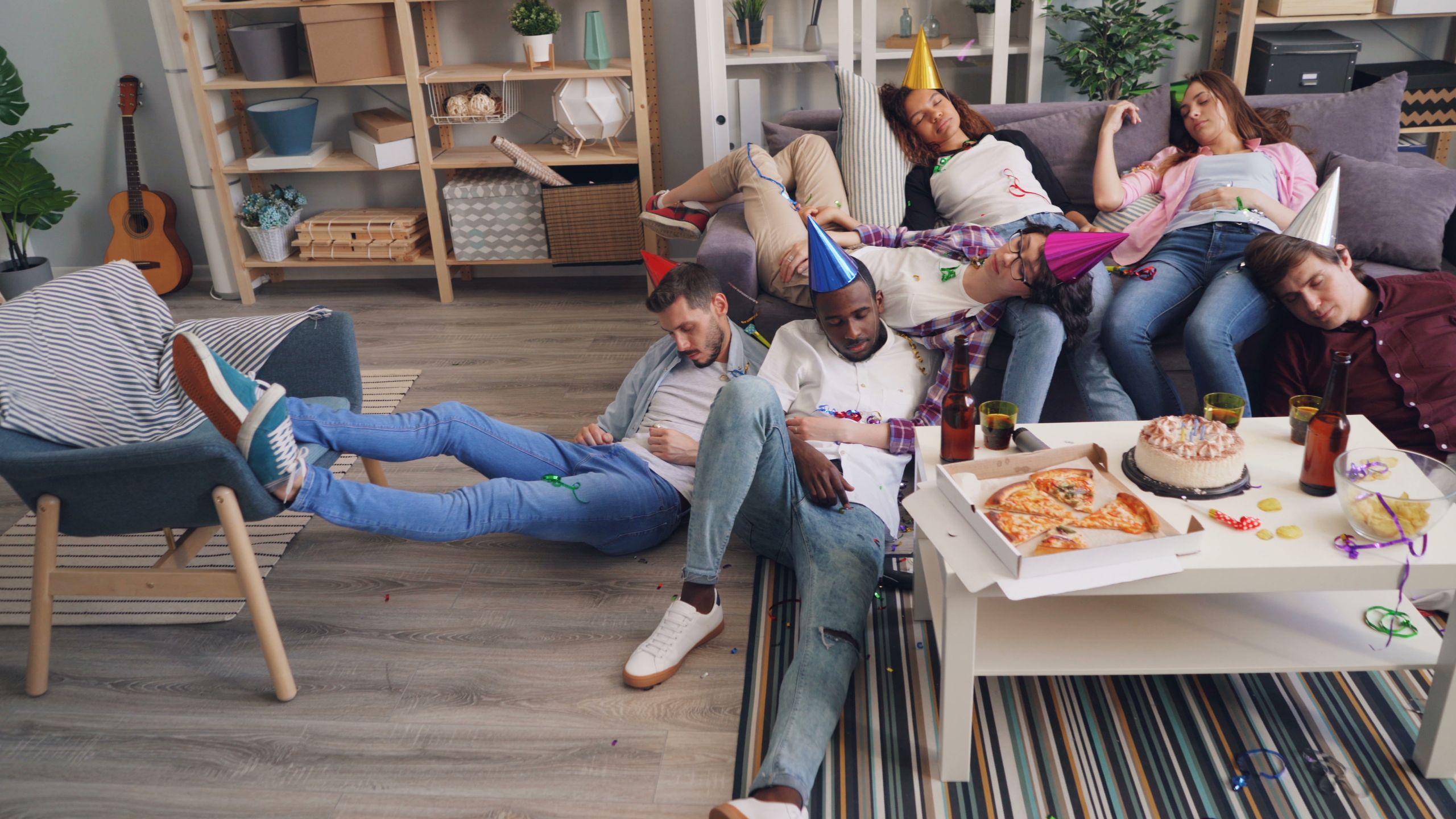 Group of friends sleeping after a lively indoor party with food and decorations.