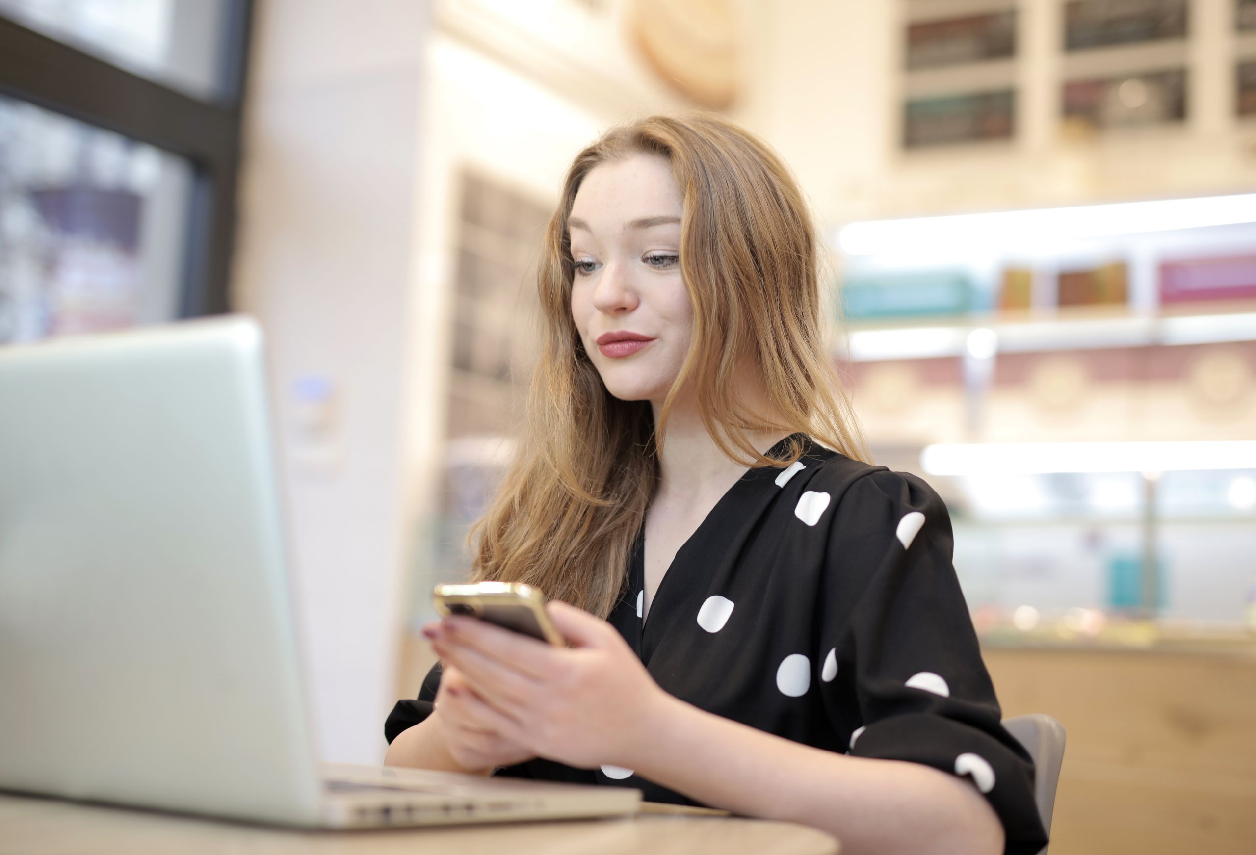 Smiling young woman multitasking with phone and laptop in stylish home office.