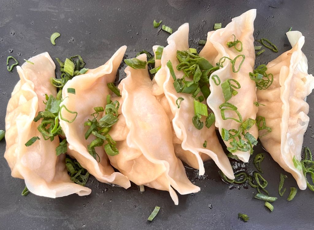 Steamed dumplings garnished with fresh scallions on a dark plate, ready to enjoy.