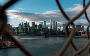 Stunning view of New York City skyline through a fence, showcasing skyscrapers and Brooklyn Bridge.