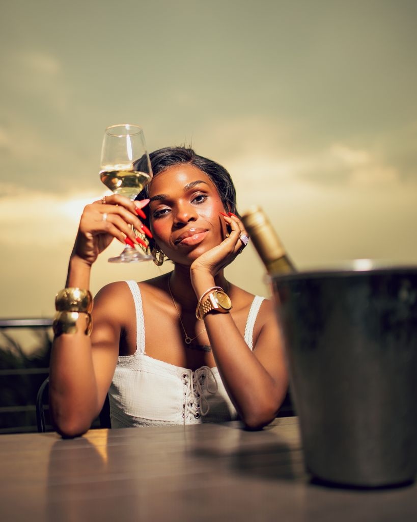 Stylish woman in a white dress savoring wine outdoors at sunset.