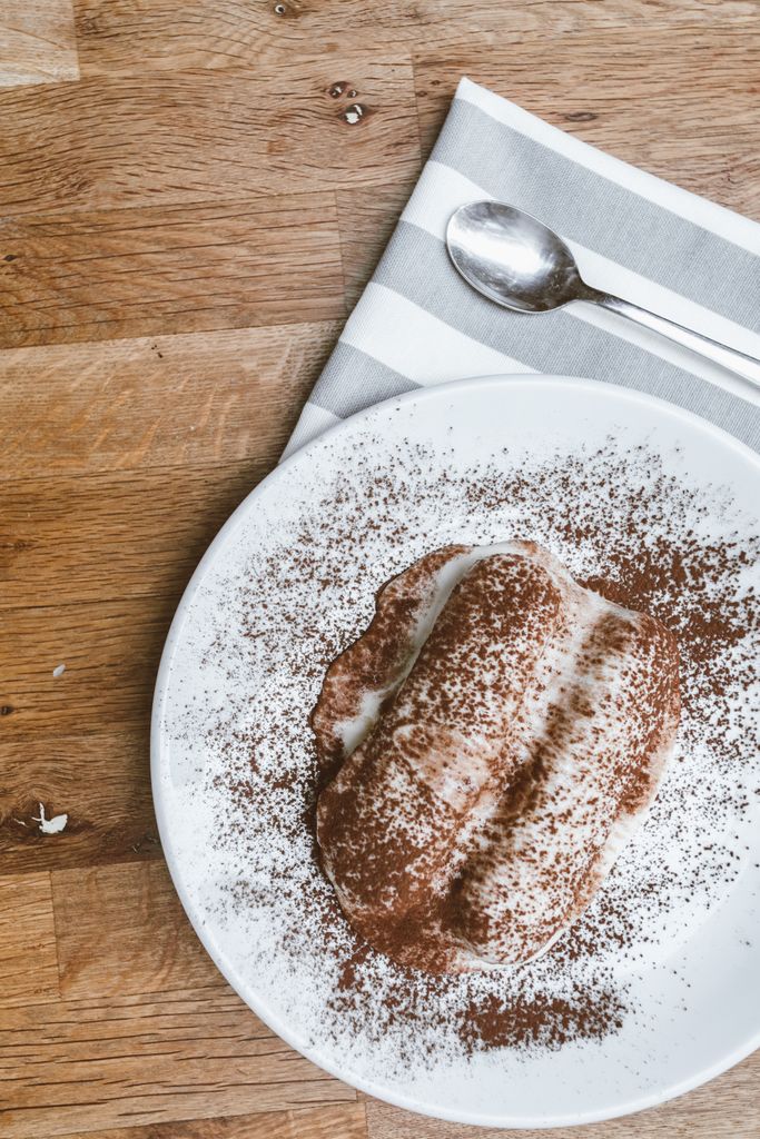 Tiramisu sprinkled with cocoa powder on a ceramic plate with spoon and napkin.