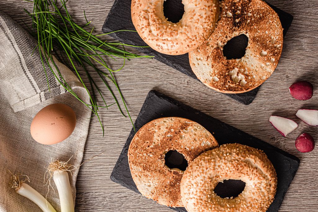Top view of toasted bagels with fresh scallions, egg, and radishes on a wooden table.