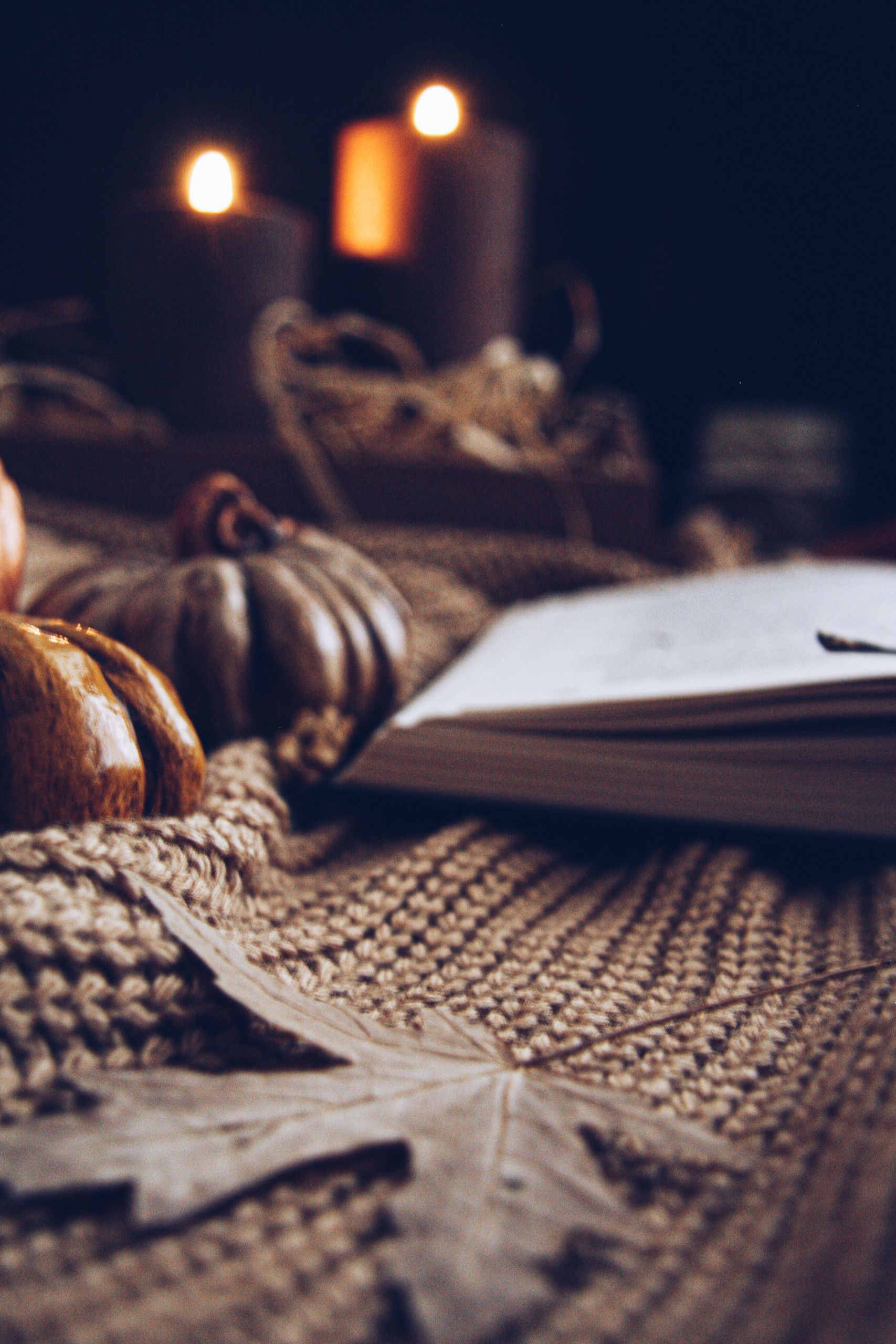 Warm autumn scene featuring candles, pumpkins, and a knitted fabric for a cozy atmosphere.