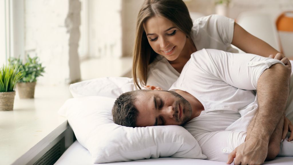 Woman smiling as man sleeps peacefully in a comfortable room.