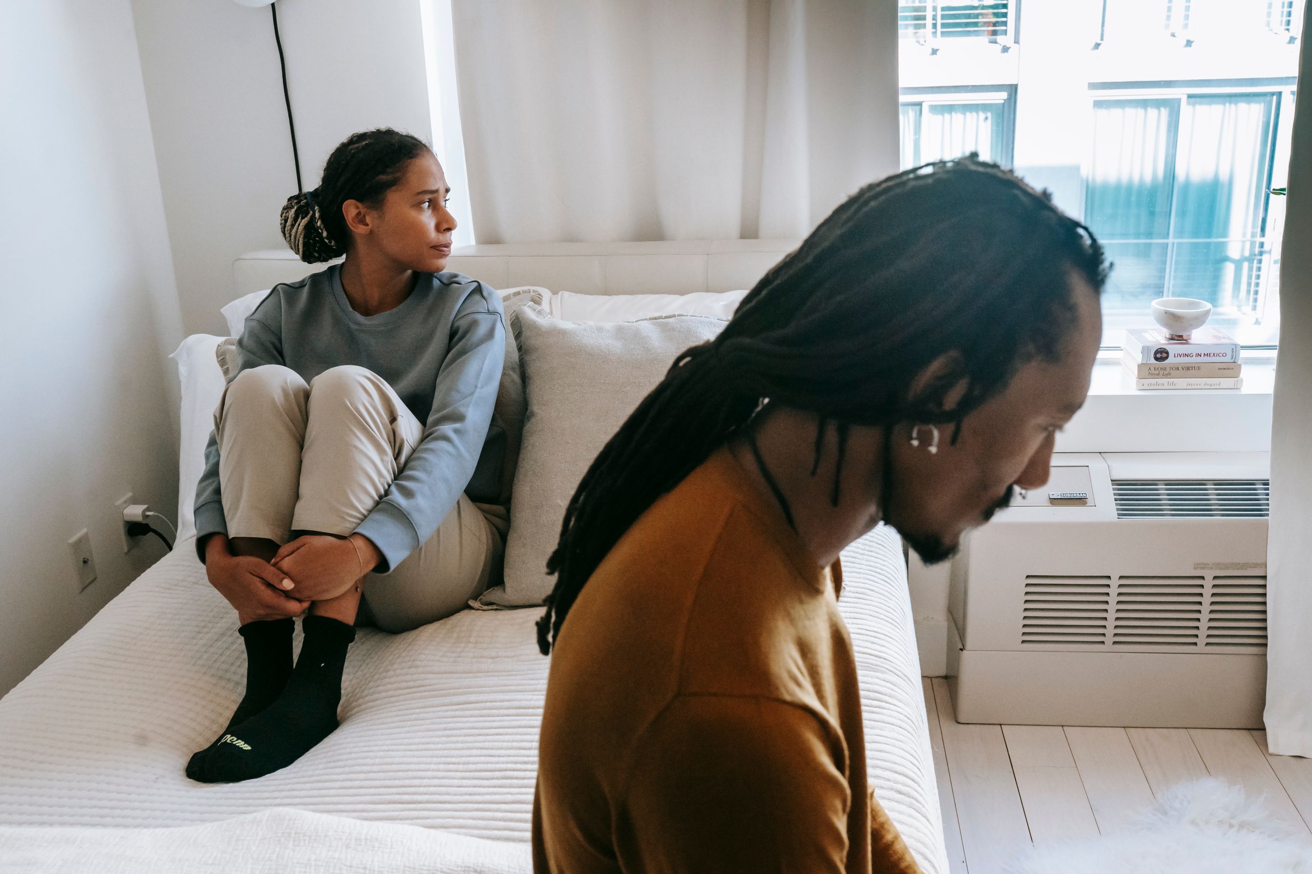 Young African American couple in casual clothes resting on bed with sad face in daytime