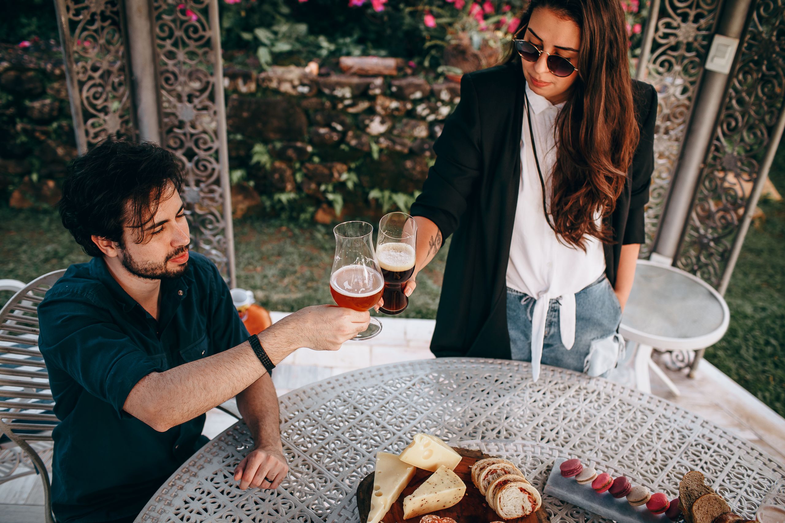 A couple enjoying an outdoor brunch with beer and cheese. Relaxed, stylish setting with a gourmet spread.