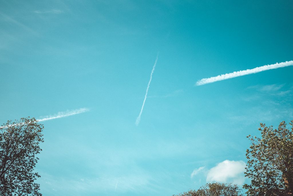 This image features a bright blue sky with visible contrails and tree tops.